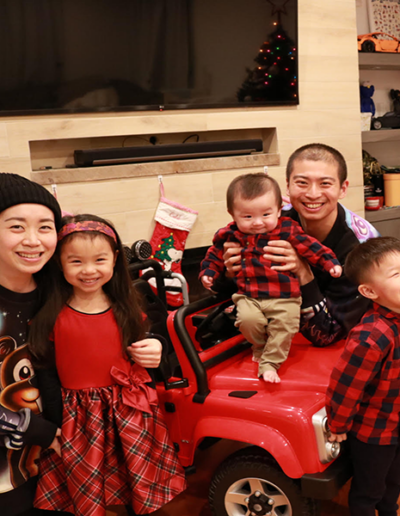 Photo of mother, father and three children in Christmas clothing smiling happily together